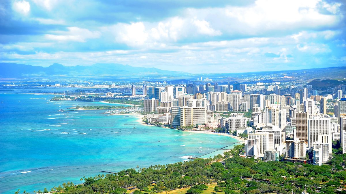 Aerial view of Honolulu and Waikīkī coastline with high-rise buildings, turquoise waters, and lush green parks.