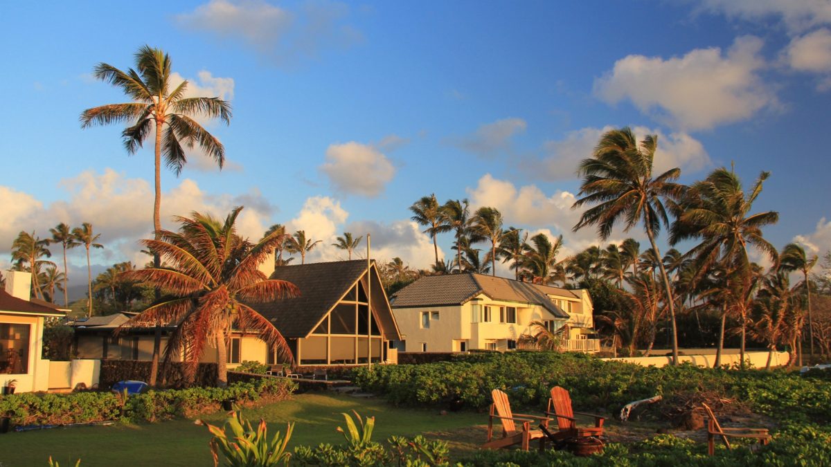 Coastal Oʻahu homes at sunset surrounded by palm trees, tropical plants, and open lawn seating.