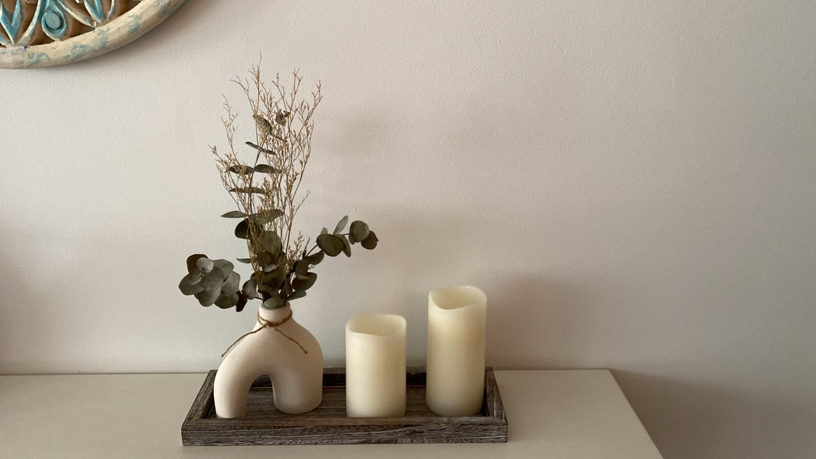 Minimalist console styling with a sculptural ceramic vase holding dried greenery, paired with two neutral candles on a wooden tray.